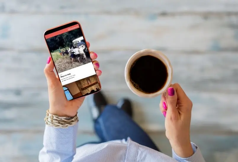 A person holding a phone displaying the YWAM Converge website