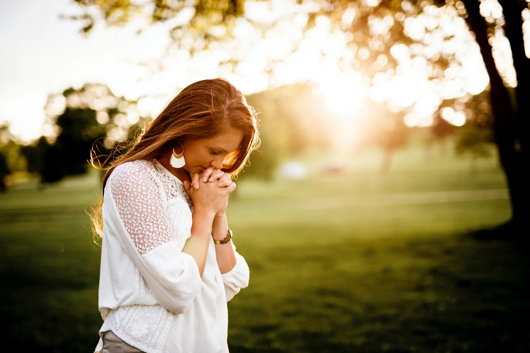 A young woman praying outdoors in warm evening light
